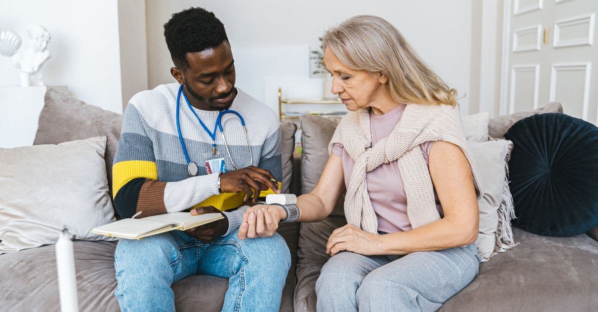Healthcare professional checking blood pressure of elderly woman in a cozy indoor setting.