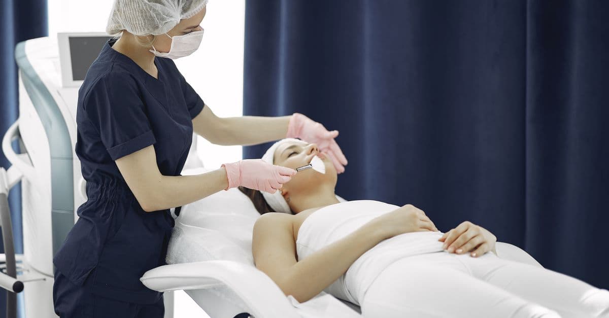 Aesthetician applying facial treatment on a relaxed woman in a modern spa clinic setting.