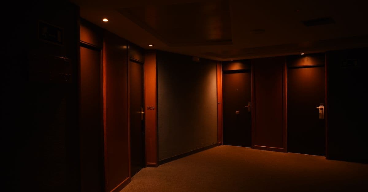 A dark, quiet hotel corridor featuring multiple closed wooden doors and soft lighting.