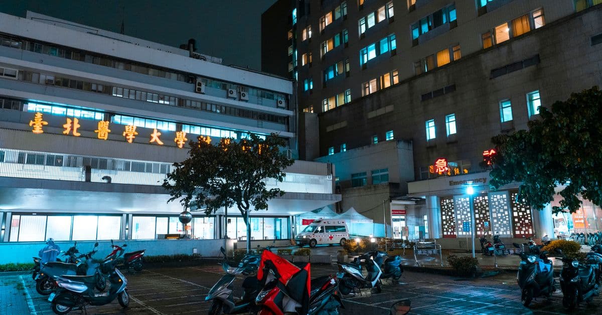 Night view of a hospital with scooters parked outside, illuminated by bright city lights.