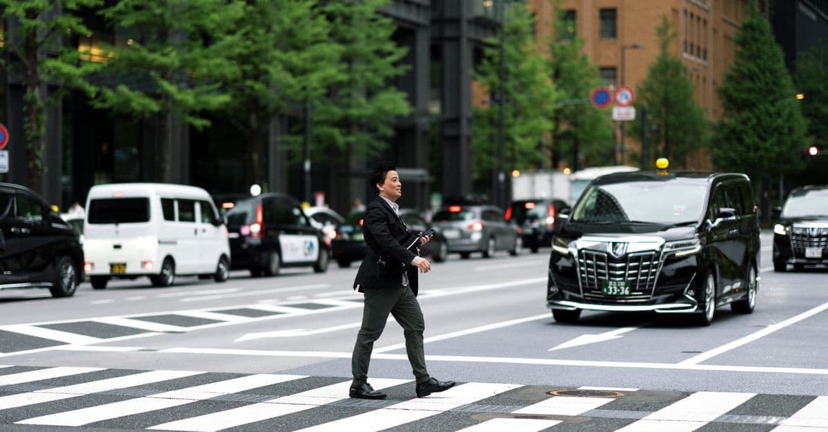 A businessman walking across a busy city street in Japan with vehicles in the background.